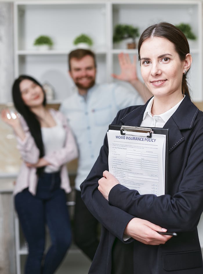 Services-03 A smiling businesswoman holding a home insurance policy with clients in the background.